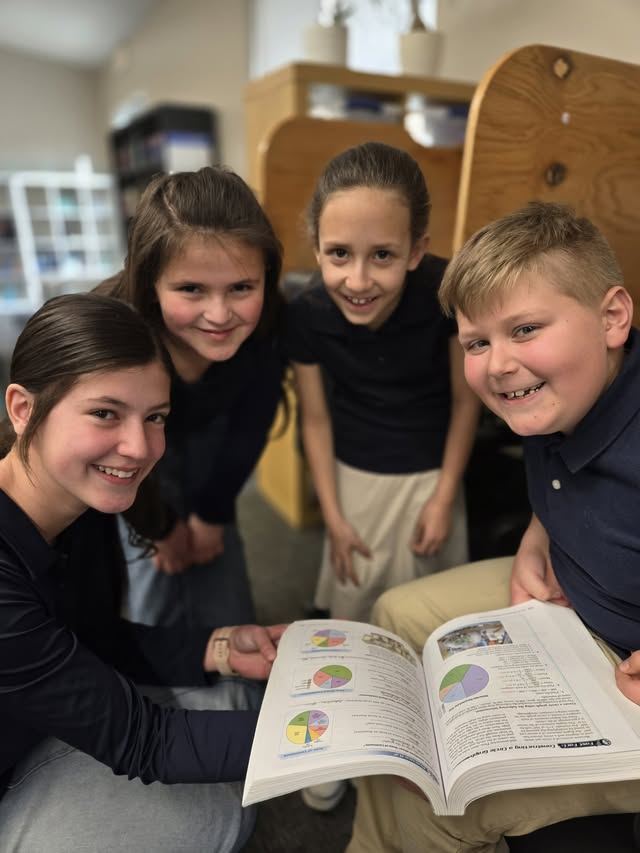 Students gathered around an open book, smiling