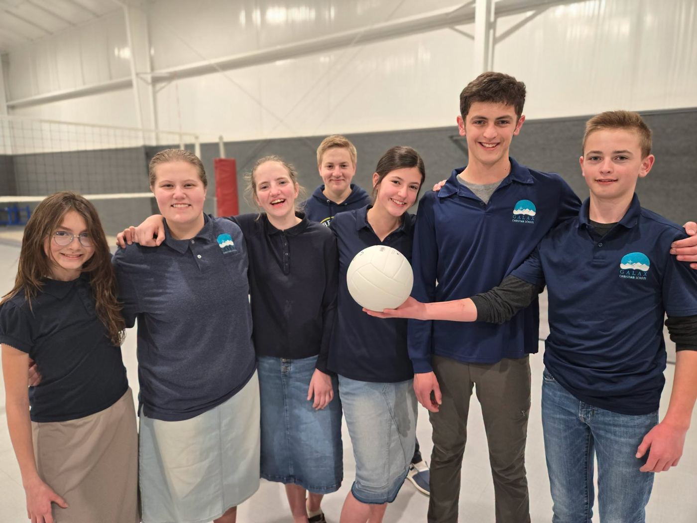 The GCS volleyball team holding a volleyball in the gym